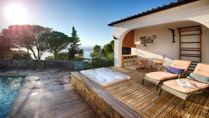 A wooden deck with a hot tub, lounge chairs, and a view of the sea.