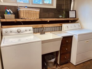 Ein Waschbereich mit Waschmaschine, Trockner, Spüle und einem Korbwäscheschrank auf einem Holzregal.