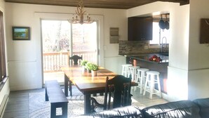 Un coin repas avec une table en bois, des chaises et un banc. Il y a également un coin cuisine avec un mur recouvert de pierres et un porte-ustensiles suspendu.