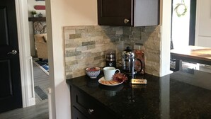 Une cuisine avec un mur recouvert de pierres, une machine à café, une tasse et une assiette remplie de biscuits.