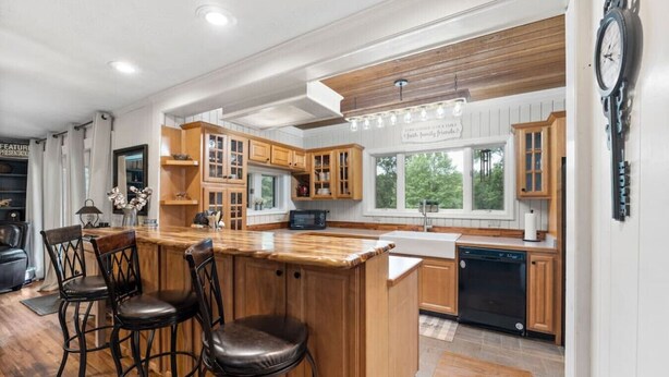 A kitchen with wooden cabinets, a bar area with stools, and a dishwasher. - Refuge Ranch Lodge | Log Cabin | Lake | Privacy | Weddings (Locust Grove)