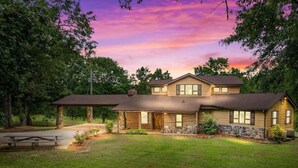A two-story house with a stone foundation, a covered patio, and a well-maintained lawn. - Refuge Ranch Lodge | Log Cabin | Lake | Privacy | Weddings (Locust Grove)