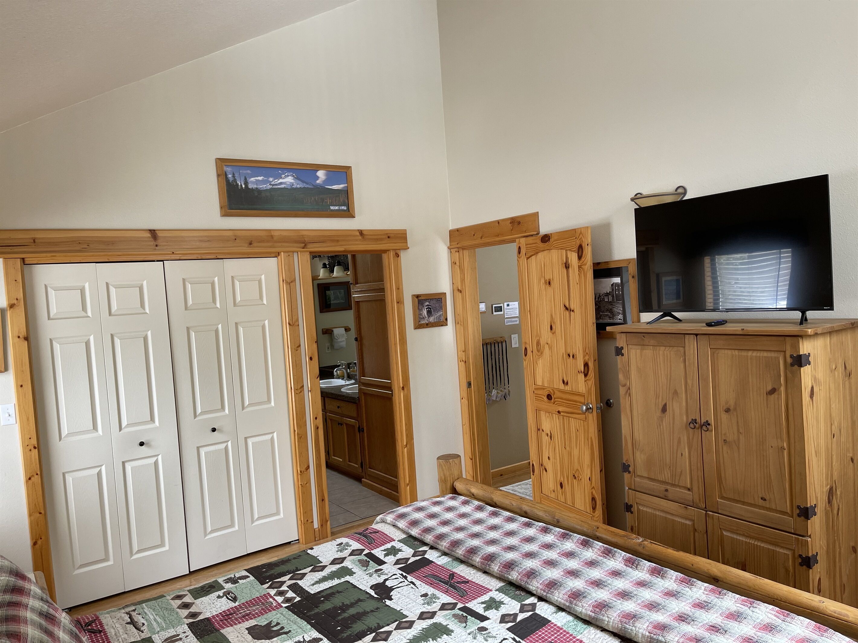 A bedroom with a bed, a wooden wardrobe, a television, and a framed picture on the wall.