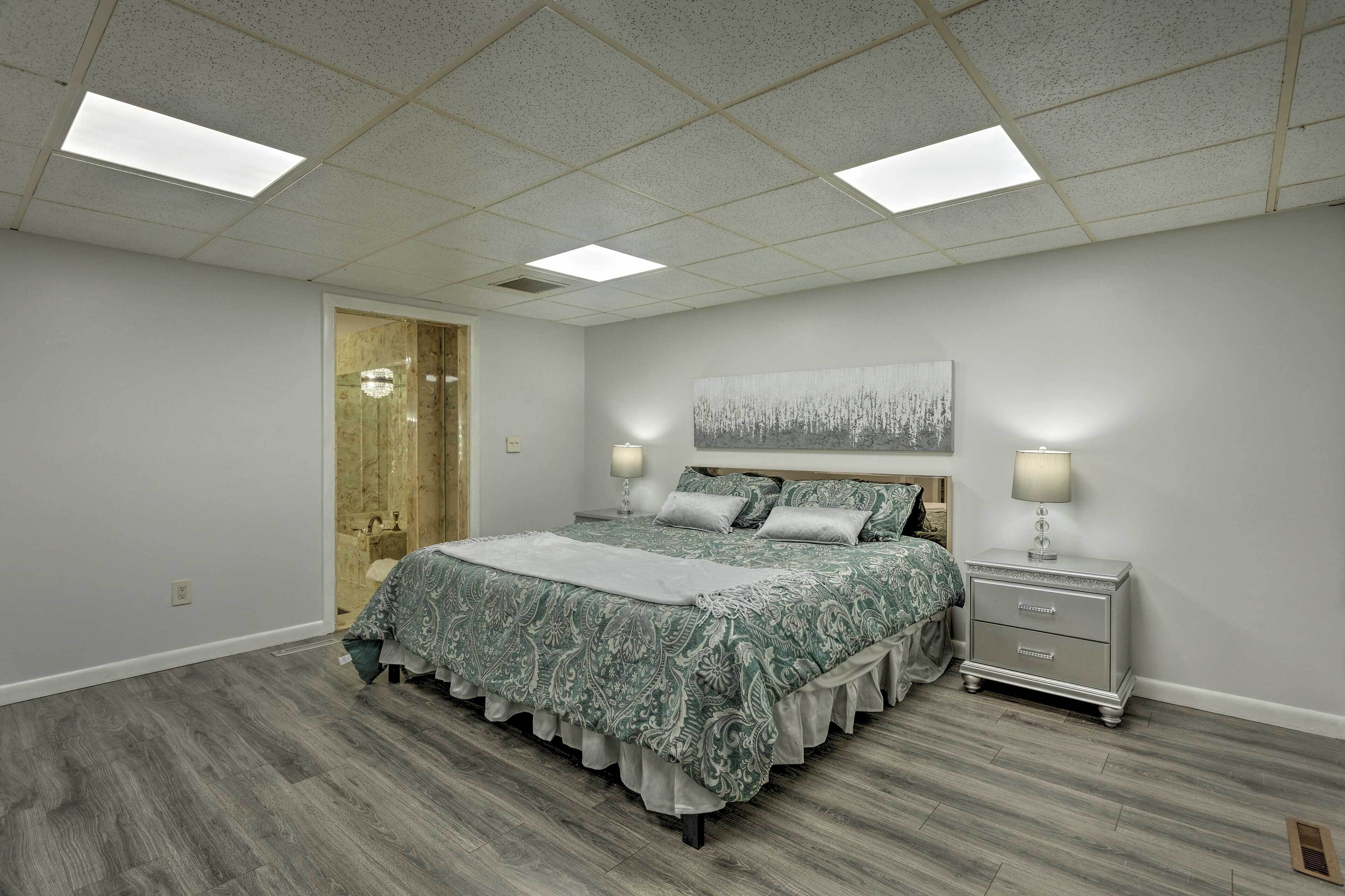 A bedroom with a bed, bedside tables, a nightstand, a painting, and a skylight.