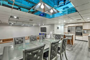 Una sala de conferencias moderna con una mesa de cristal, sillas de cuero, una zona de cocina con electrodomésticos y un techo con diseño reflectante.