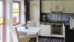 A compact kitchen with white cabinets, a built-in oven, and a dining area with a white table and chairs. - Chalet in Krimml near Waterfalls (Krimml)