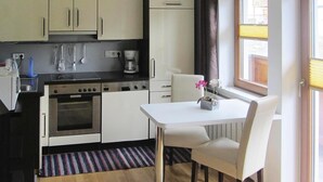 A compact kitchen with white cabinets, a built-in oven, and a small dining table with chairs. - Chalet in Krimml near Waterfalls (Krimml)