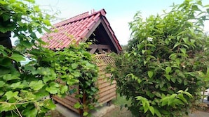 Ein kleines Holzgebäude mit geneigtem Dach, umgeben von üppigem Grün.