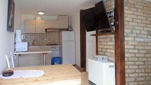 Eine kleine Küche mit einem Holztisch, einem weißen Kühlschrank und einem an einer Backsteinwand montierten Fernseher.