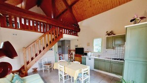 A spacious living area with a dining table, chairs, a sofa, a staircase, and a kitchen with green cabinets and a tiled backsplash.