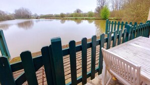 A calm lake with a wooden deck and a table and chair in the foreground.