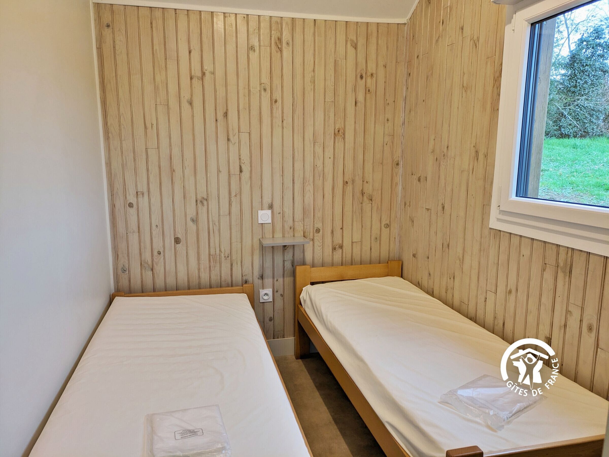 Een kleine, eenvoudige kamer met houten lambrisering, een raam en twee eenpersoonsbedden.