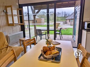 A dining area with a table set for two, a basket of croissants, and a view of the outdoor patio.