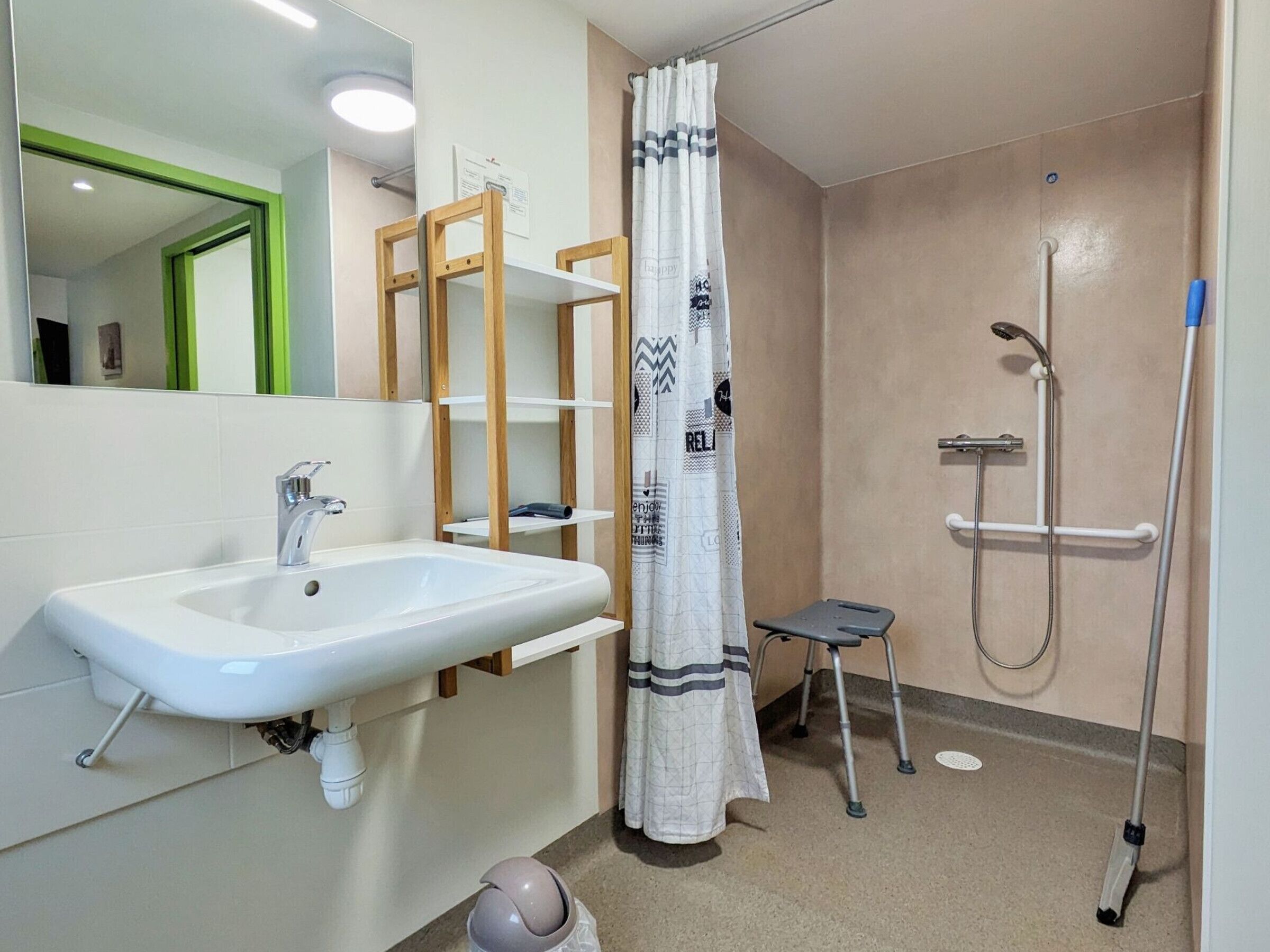 A bathroom with a white sink, a shower with a handheld showerhead, a step stool, and a towel rack.
