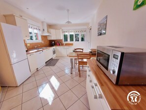 A modern kitchen with white cabinets, a stainless steel microwave, and a dining area with wooden chairs and a table.