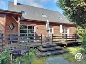 A wooden cabin with a deck, outdoor seating, and a barbecue grill.