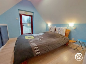 A bedroom with a sloped ceiling, a bed with a patterned bedspread, a window with a view, and a small table by the bed.
