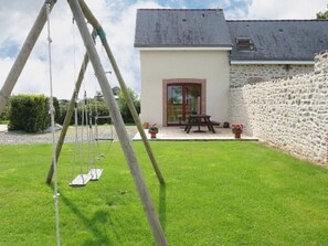 En baghave med et gyngestativ, en stenvæg, et picnicbord og en bygning med en røddør.