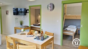 A compact room with a dining table, chairs, a television, a clock, and a bunk bed.