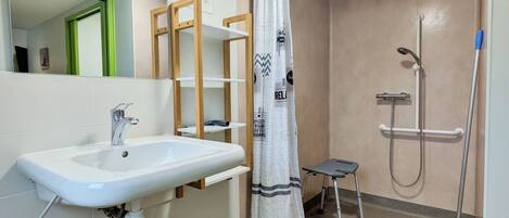 A bathroom with a white sink, a shower with a handheld showerhead, a step stool, and a towel rack.