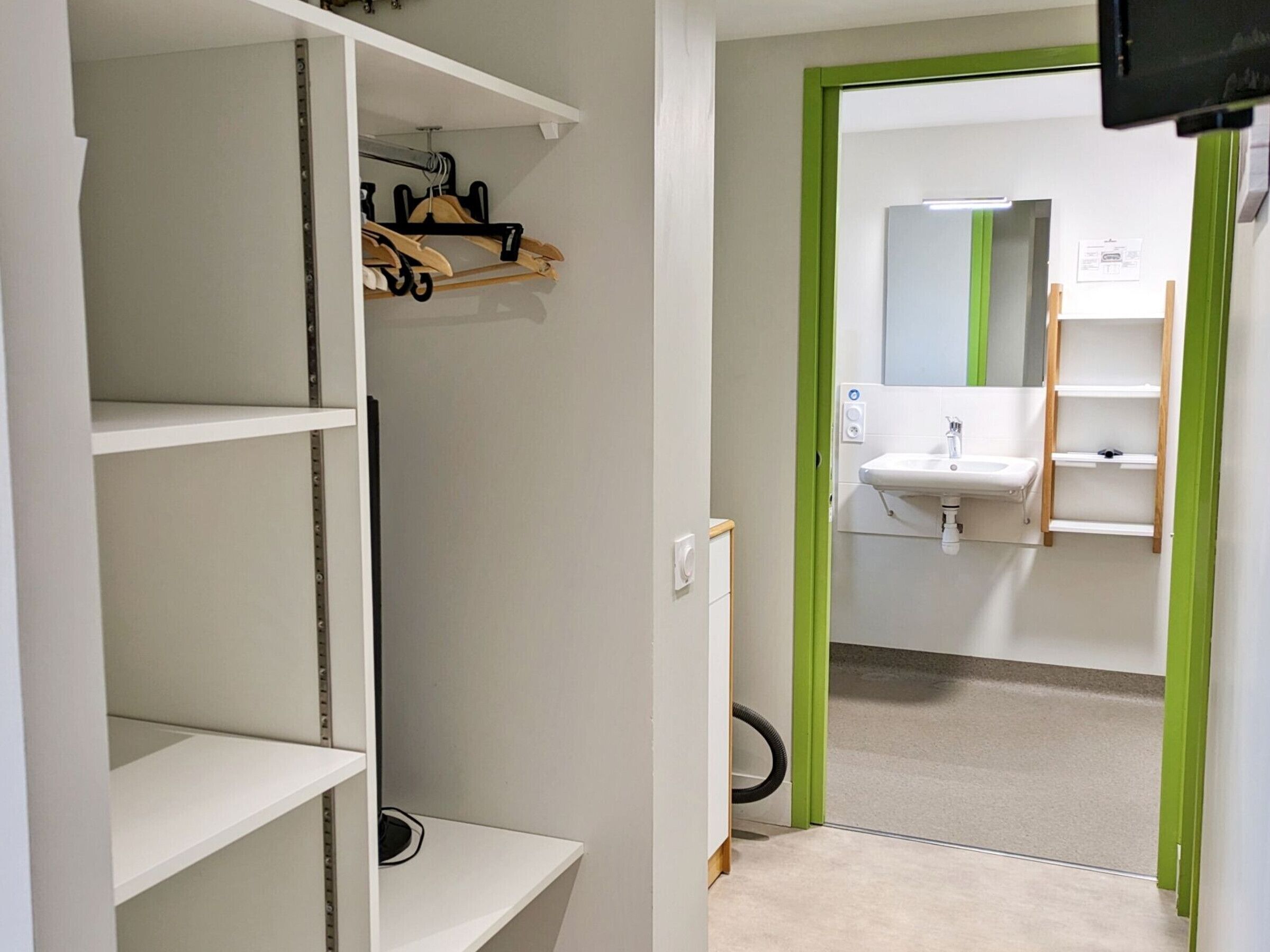 En gang med et spejl med grøn ramme, en vask og en hylde med knager.
