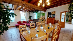 A cozy living room with a wooden dining table set for four, a red sofa, and a kitchen in the background. - Spacious Family Home with Heated Indoor Pool, Billiards, and Scenic Terraces (Carelles)