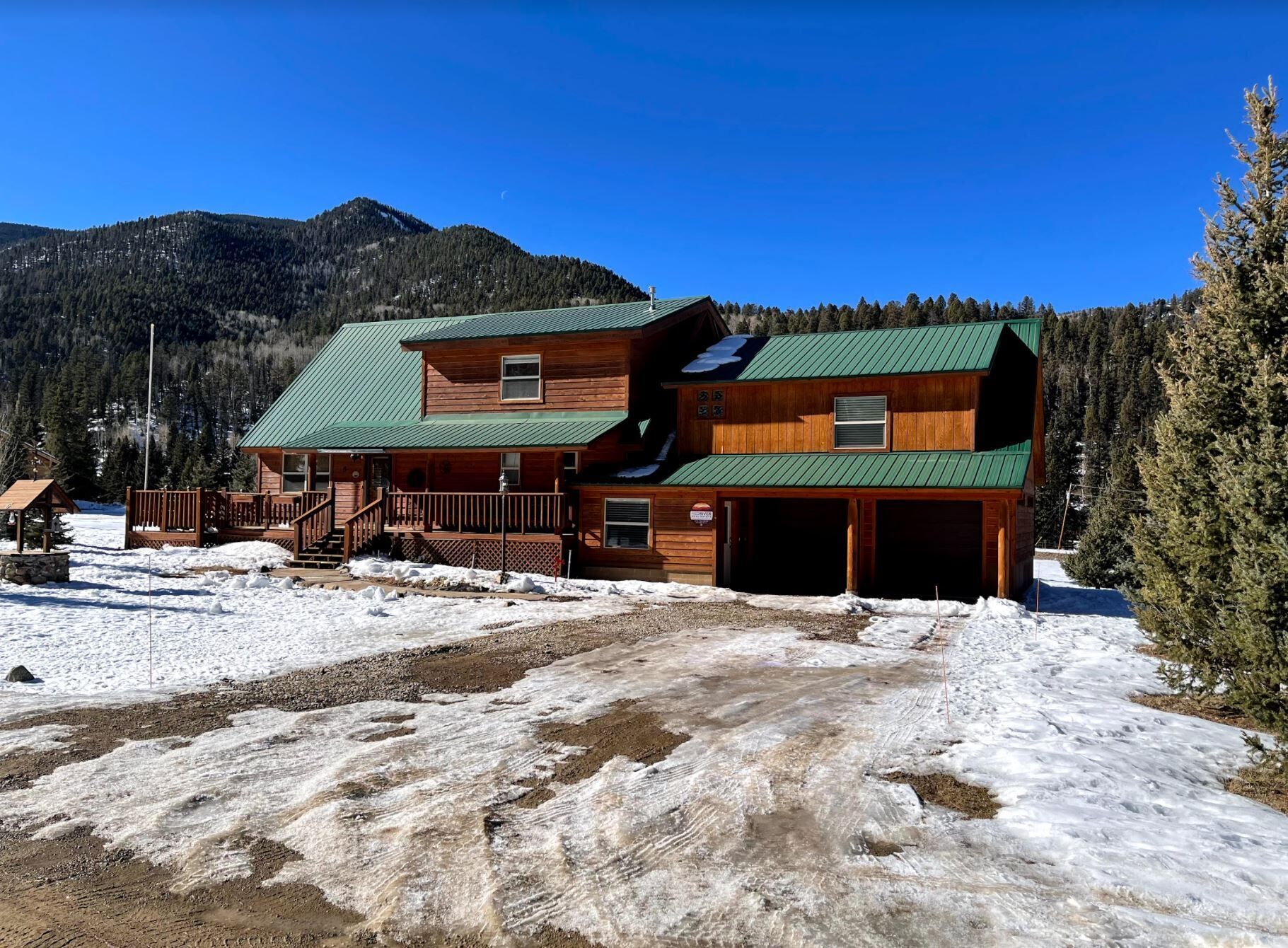 A two-story log cabin with a green roof, a covered front porch, and a garage.