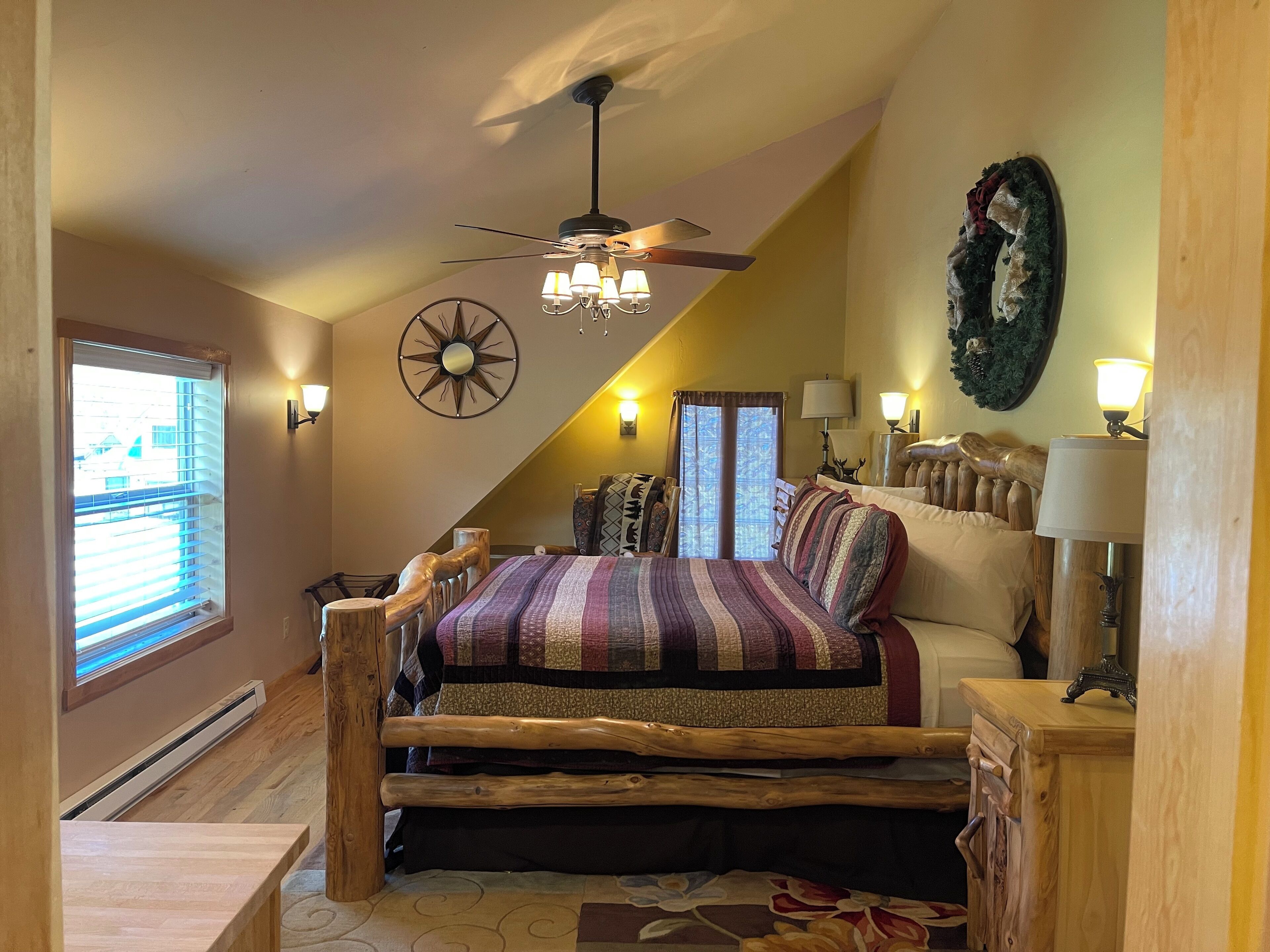 A bedroom with a sloped ceiling, a bed with a wooden frame, a ceiling fan, and a chandelier.