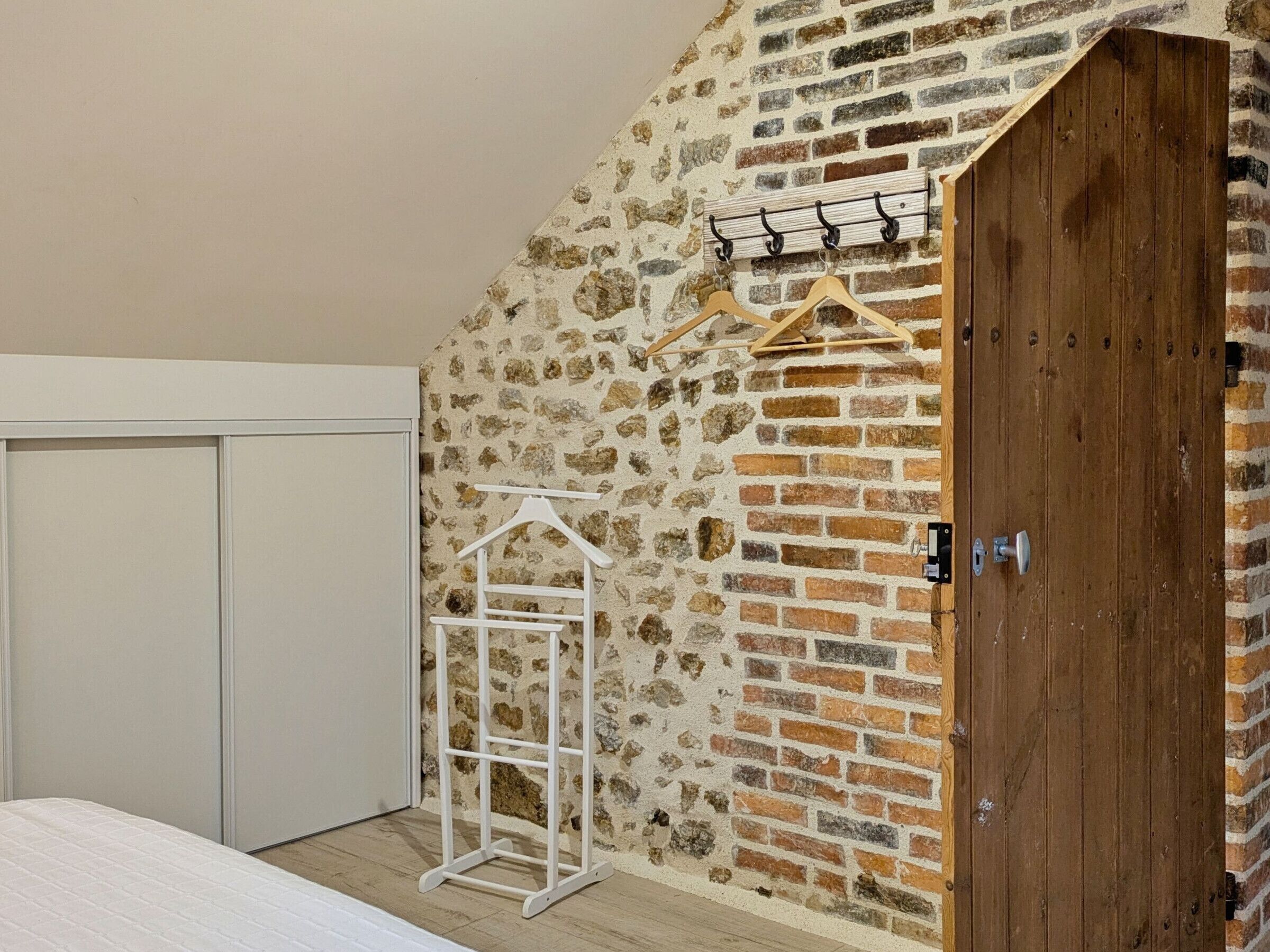 A bedroom with a stone wall, a wooden door, and a white wardrobe.