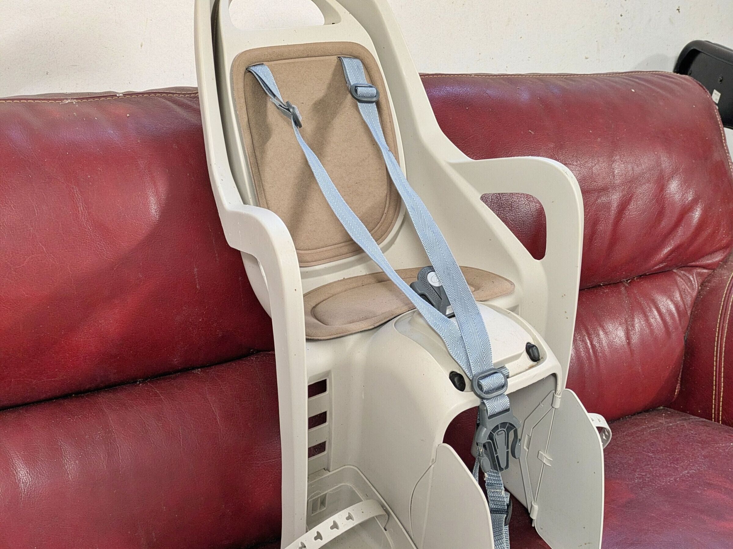 A child car seat attached to a red leather couch.