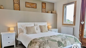 Ein Schlafzimmer mit einem großen Bett, zwei Nachttischen, einem Fenster und Wanddekorationen.