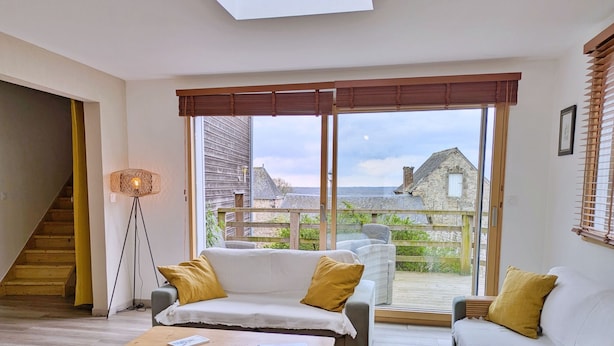 Ein geräumiges Wohnzimmer mit einem großen Schiebeglastür, die auf einen Balkon führt, einer Sofagarnitur, einer Stehlampe und einer Treppe.