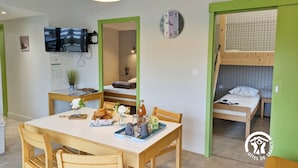 Une pièce de taille modeste comprenant une table à manger, des chaises, un téléviseur, une horloge et un lit superposé.