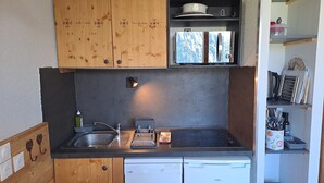 Eine kompakte Küche mit Holzschränken, einem eingebauten Geschirrspüler, einem Herd und einem kleinen Fenster.