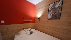 Ein Einzelbett mit weißer Matratze und Kissen, eine rote Wand, ein Holz-Kopfbrett und ein Bild von einem Reh an der Wand.
