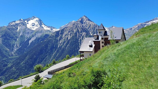 Eine Berglodge mit Parkplatz, einer Treppe, die zum Gebäude führt, und Blick auf schneebedeckte Gipfel.