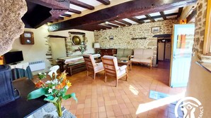 Un intérieur rustique avec des poutres apparentes, des murs en pierre, un coin repas avec des meubles en bois et un téléviseur.