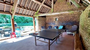 Un espace extérieur abrité comprenant une table de ping-pong, des chaises et un mur en pierre.