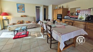 Ein gemütliches Wohnzimmer mit einer Couch, einem Esstisch für zwei Personen und einer Küchenzeile mit Holzschränken und einer gefliesten Spritzschutzleiste.