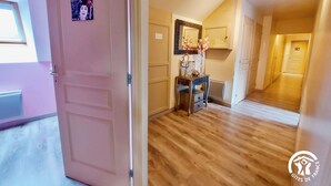 A hallway with wooden flooring, a pink door, and a mirror above a small table with a vase. - Spacious 6-Bedroom Cottage with Fishing Pond, Games & Garden - Sleeps 12-15 (Carelles)