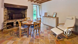 Un interno rustico con camino in pietra, tavolo da pranzo in legno e una poltrona bianca.