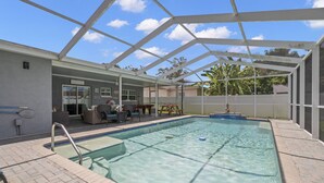 An indoor swimming pool with a covered patio area, seating, and a view of the surrounding landscape. - Quiet, Centrally Located Home w/ Heated Pool, Gas Grill & Private Backyard - Poolside Paradise (Pinellas Park)