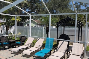 A covered outdoor area with lounge chairs and a barbecue grill.