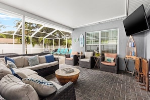 A covered outdoor seating area with wicker furniture, a flat-screen TV, and a brick floor. - Heated Pool, Private Backyard ~ Poolside Paradise (Pinellas Park)