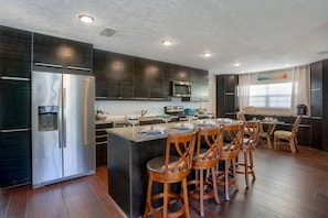 A modern kitchen with dark cabinetry, stainless steel appliances, and a central island with bar stools. - Heated Pool, Private Backyard ~ Poolside Paradise (Pinellas Park)