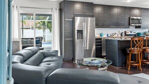 A modern kitchen with dark cabinets, a stainless steel refrigerator, and a glass coffee table. - Quiet, Centrally Located Home w/ Heated Pool, Gas Grill & Private Backyard - Poolside Paradise (Pinellas Park)