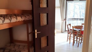 A room with a bunk bed, a wooden door with a handle, a dining table with chairs, and a view of trees through a window. - Quiet studio in Deux Alpes, ski access, pets allowed (Les Deux Alpes)