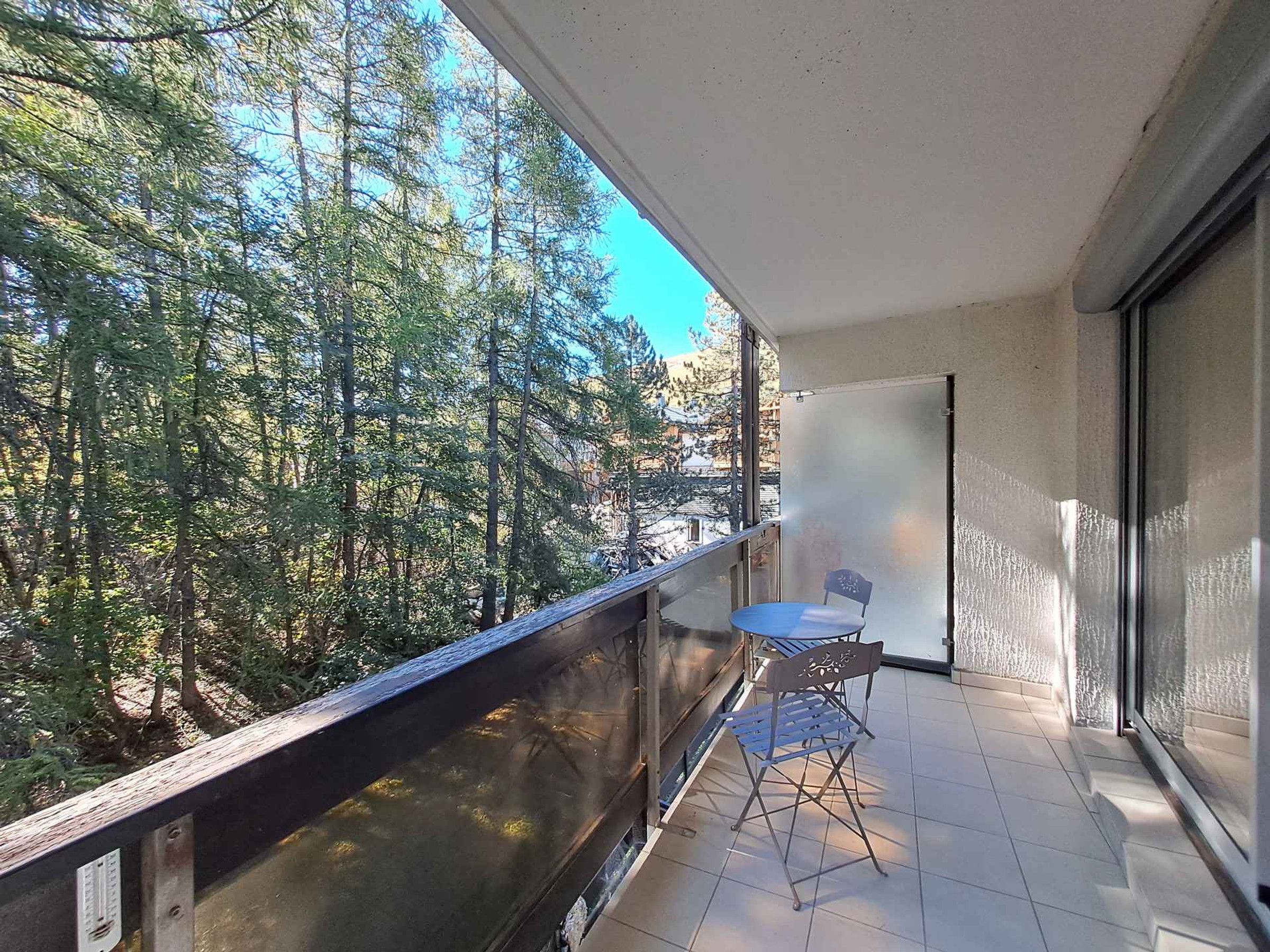 A balcony with a view of trees, a chair, and a white door.