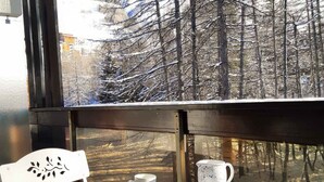 A round table with a white chair, a white cup, a white mug, and a white teapot on a balcony with a view of a snow-covered forest. - Quiet studio in Deux Alpes, ski access, pets allowed (Les Deux Alpes)
