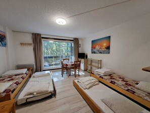 A room with two beds, a table, chairs, a TV, and a window with a view of trees. - Quiet studio in Deux Alpes, ski access, pets allowed (Les Deux Alpes)